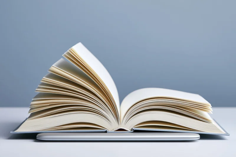 Open hardcover book with pages fanned outward resting on a closed laptop against a gray background