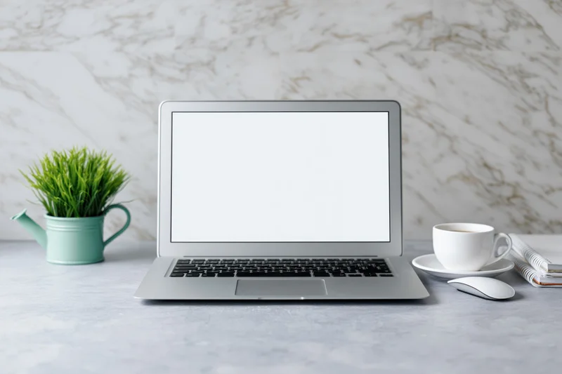 Open laptop with blank white screen centered on a clean desk with coffee cup, plant, and mouse beside it