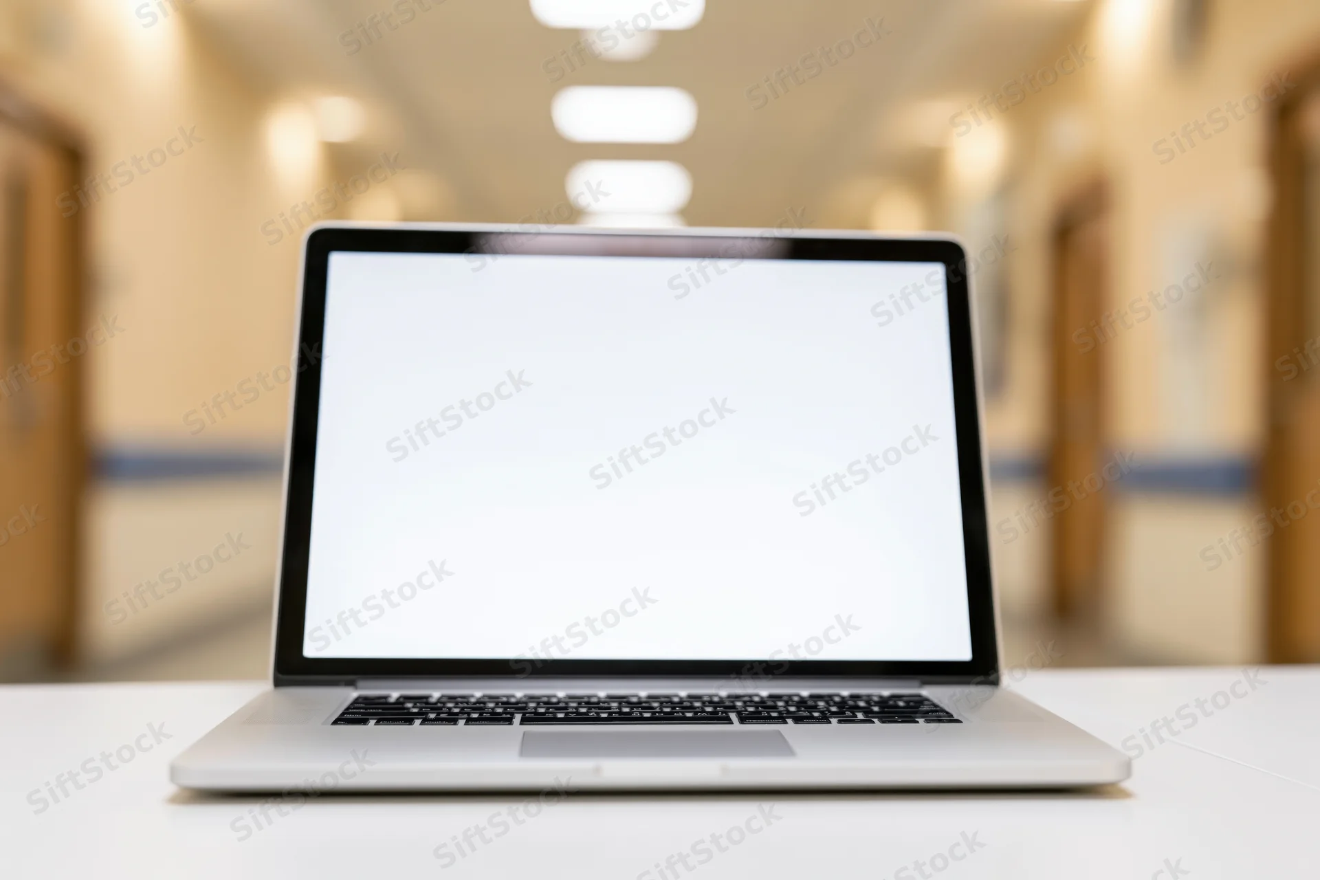 Open laptop with blank white screen on white desk in hospital hallway