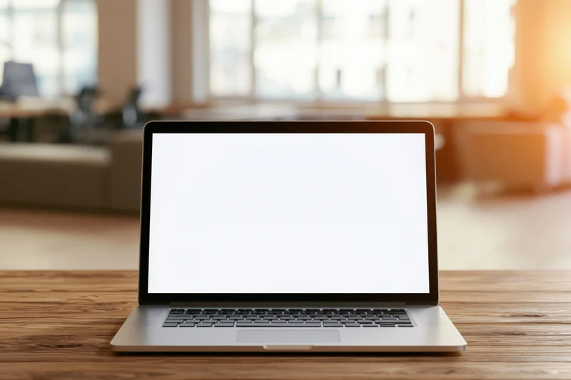 Open laptop with blank white screen on wooden desk in office space