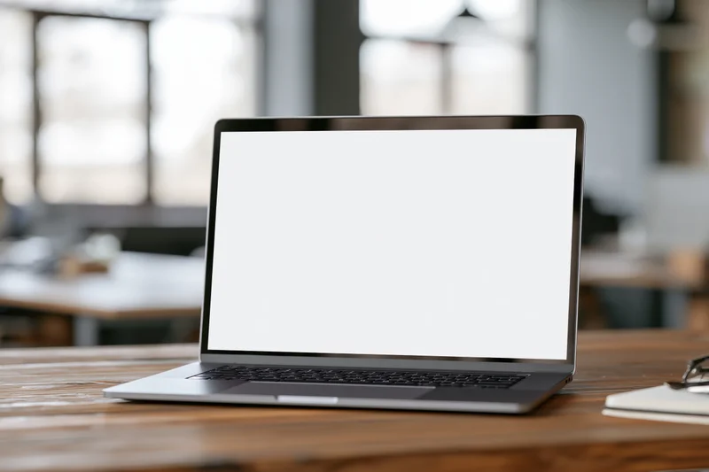 Open laptop with blank white screen on wooden desk in office workspace