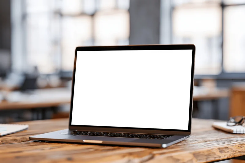 Open laptop with blank white screen on wooden desk in office workspace