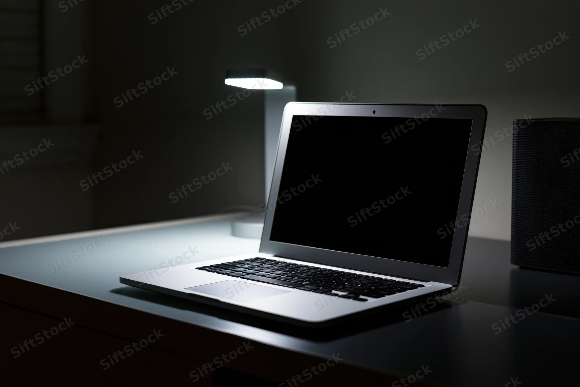 Open laptop with dark blank screen on a desk in a dimly lit room