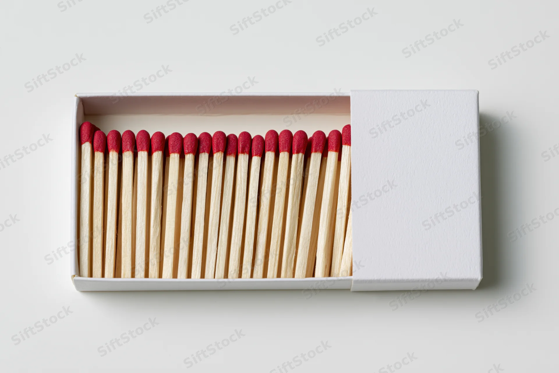 Open white matchbox with red-tipped wooden matches arranged in a row, viewed from directly above on a plain surface