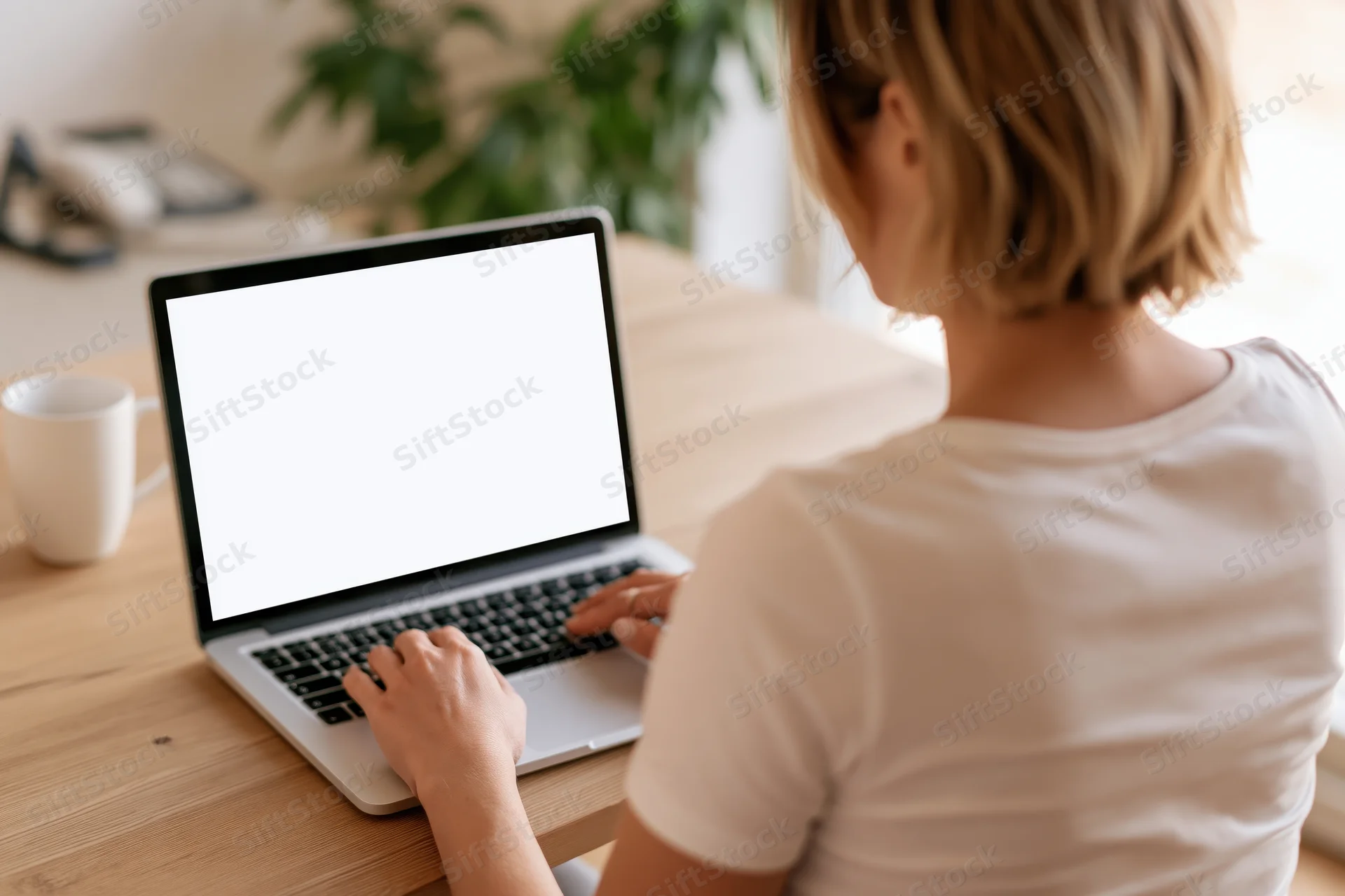 Woman typing on laptop at wooden desk from over-the-shoulder view