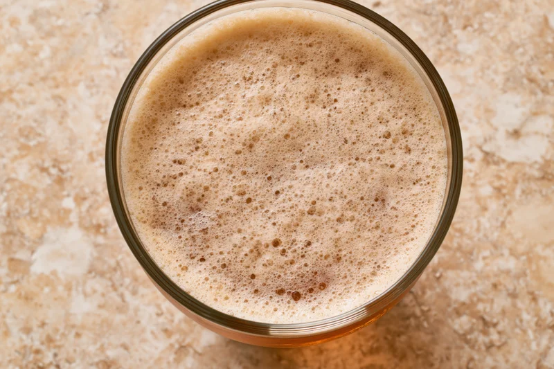 Overhead close-up of a pint glass filled with beer and foamy head on a stone countertop