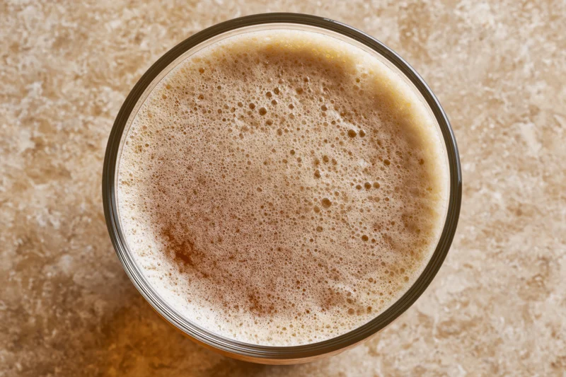 Overhead close-up of a pint glass filled with beer and foamy head on a stone countertop