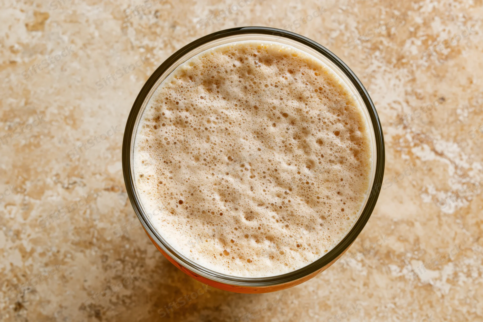 Overhead view of a pint glass filled with beer and foamy head on a stone countertop