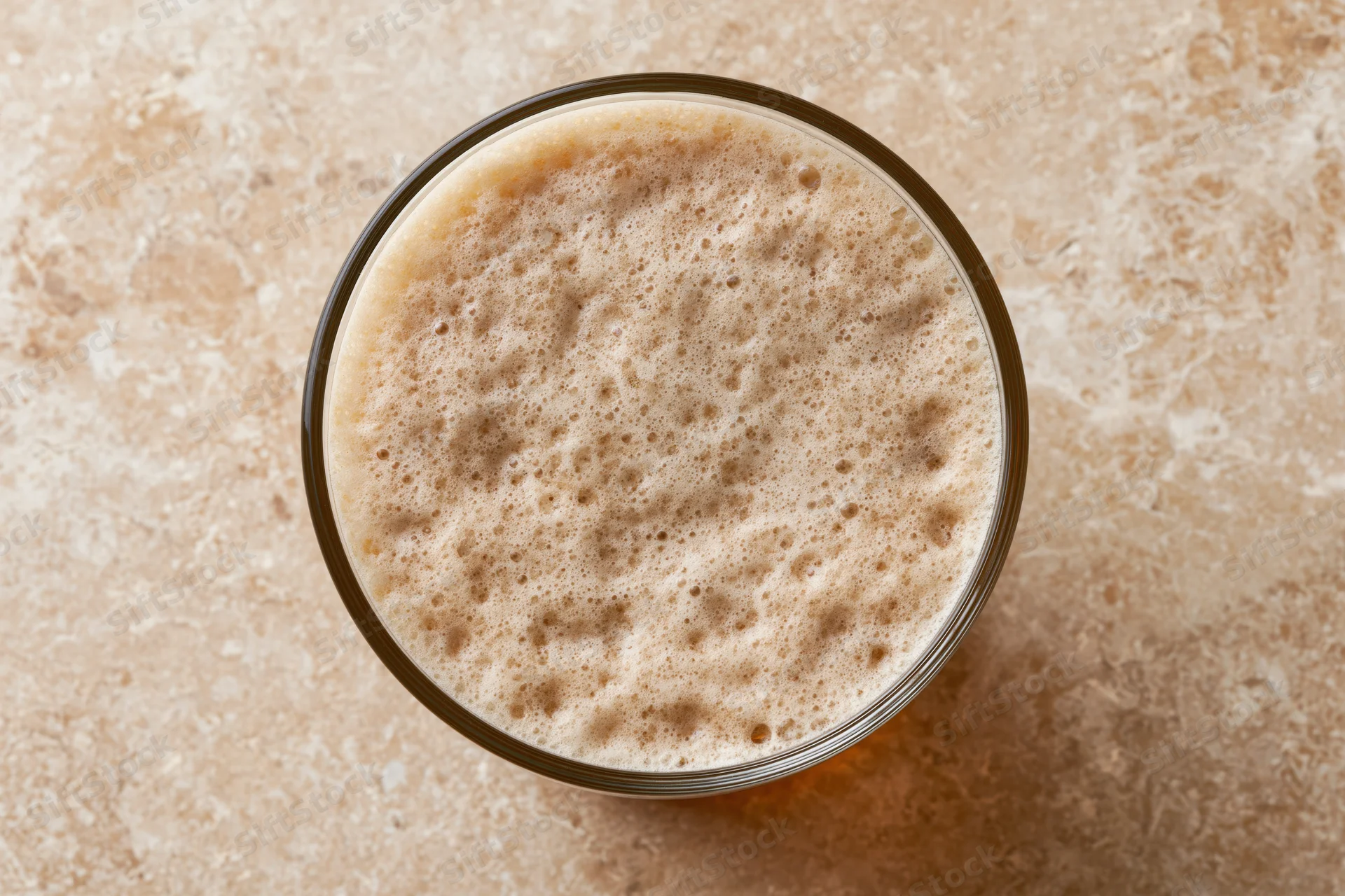 Overhead close-up of a pint glass filled with beer and foamy head on a stone countertop
