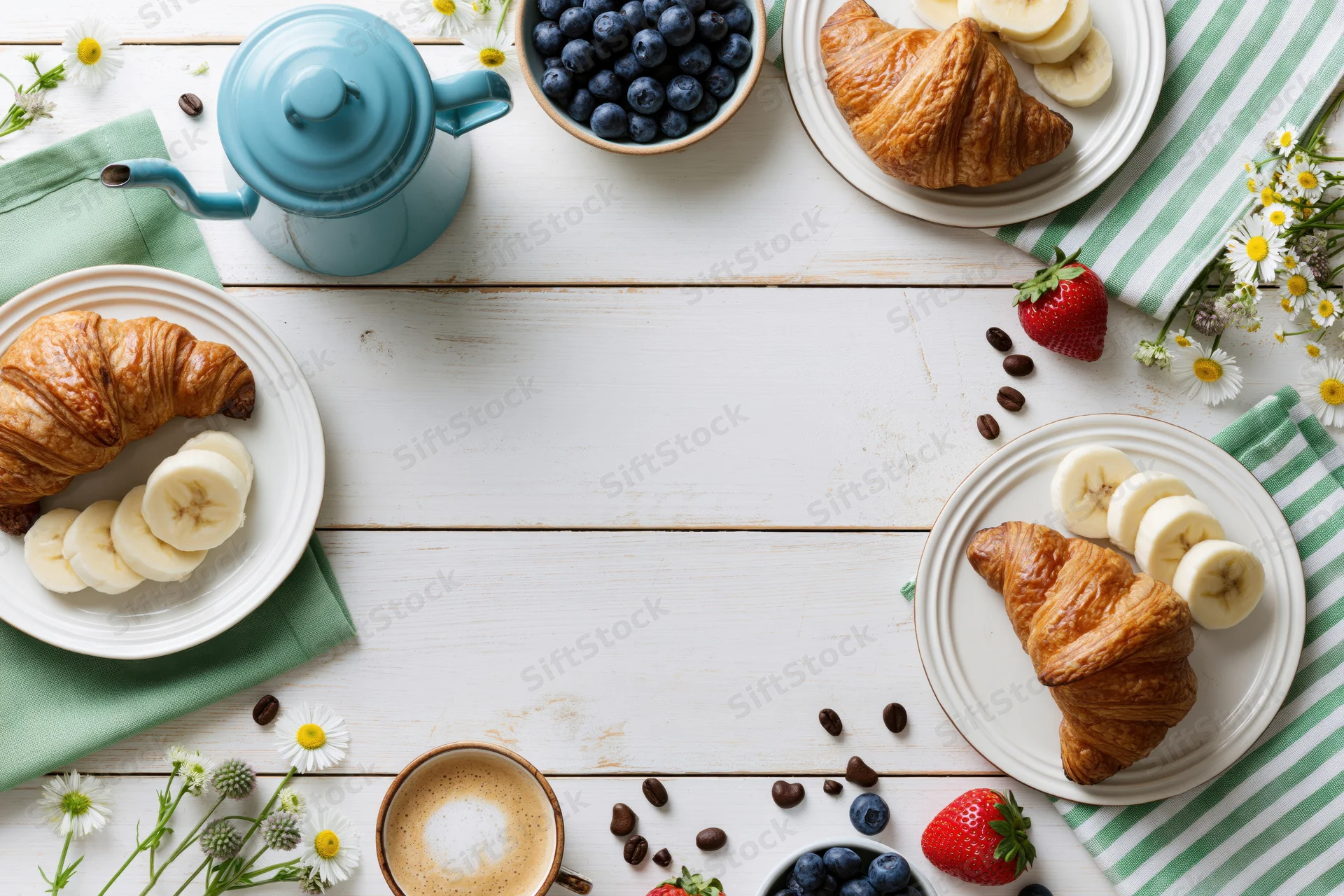 Overhead flat lay of breakfast with croissants, fruit, coffee and flowers on white wooden table