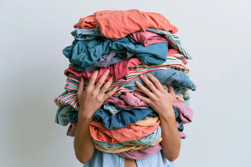 Person holding large messy pile of clothes over head against white background