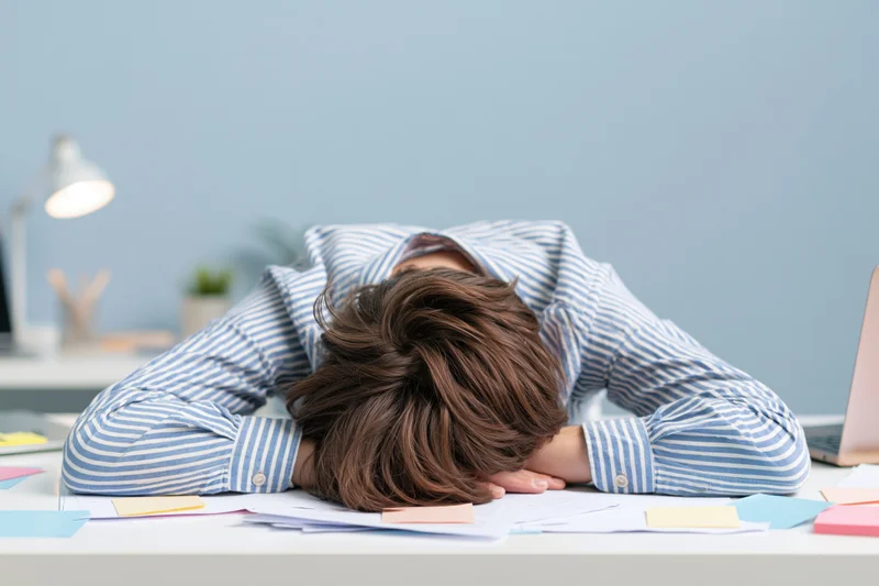 Woman slumped face-down on office desk surrounded by papers and laptop