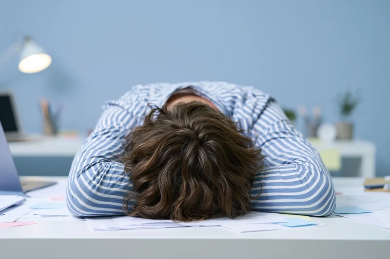 Woman slumped face-down on office desk surrounded by papers and laptop