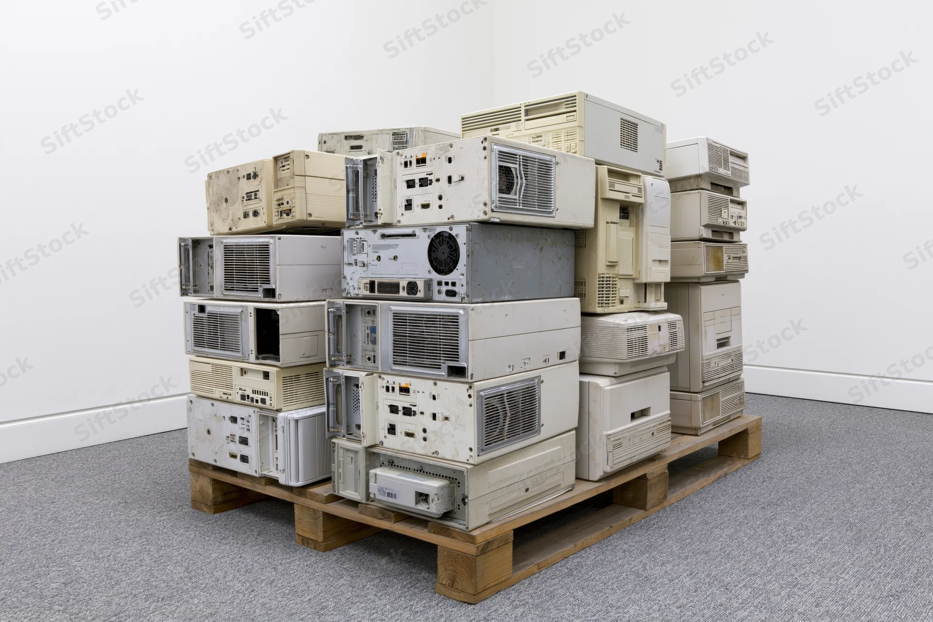 Stack of discarded desktop computer towers on wooden pallet in gallery space