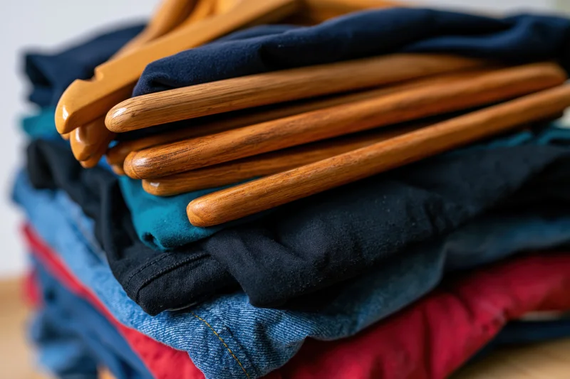 Stack of folded secondhand clothes with wooden hangers on top