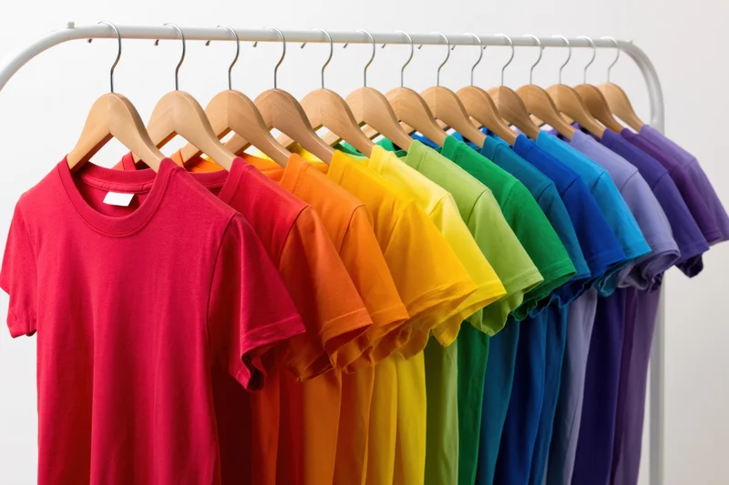 Rainbow-colored t-shirts arranged in spectrum order on a clothing rack