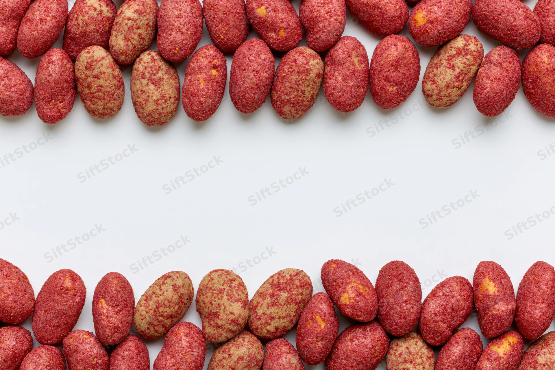 Red-coated peanuts with chili spice crust arranged in two rows on white background with copyspace