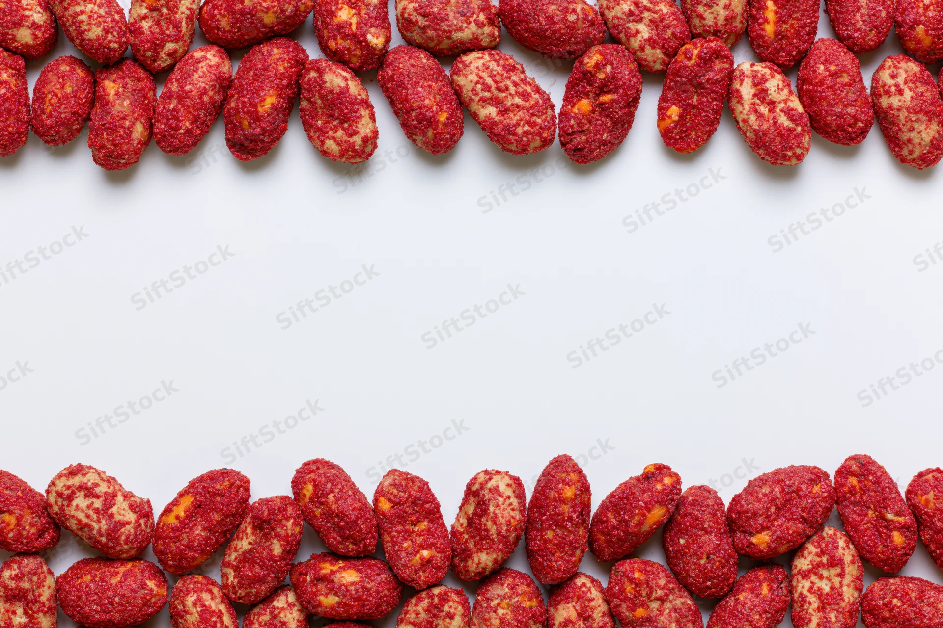 Red-coated peanuts with chili spice crust arranged in two rows at top and bottom of white surface