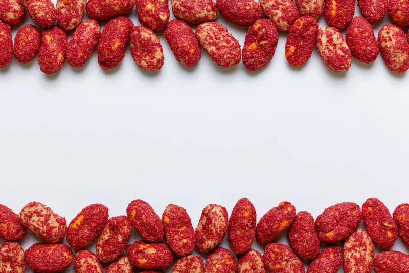 Red-coated peanuts with chili spice crust arranged in two rows at top and bottom of white surface
