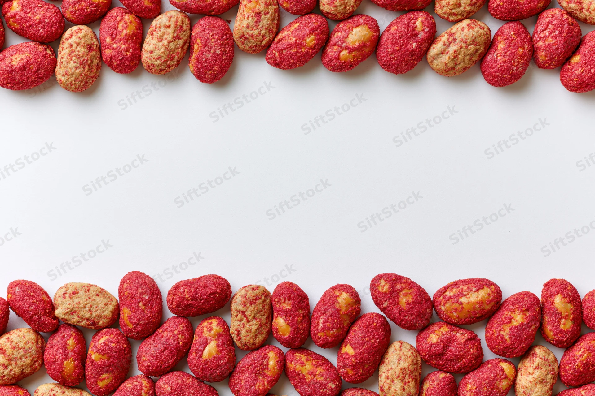 Red-coated peanuts with chili spice crust arranged in two horizontal rows on white background with copyspace
