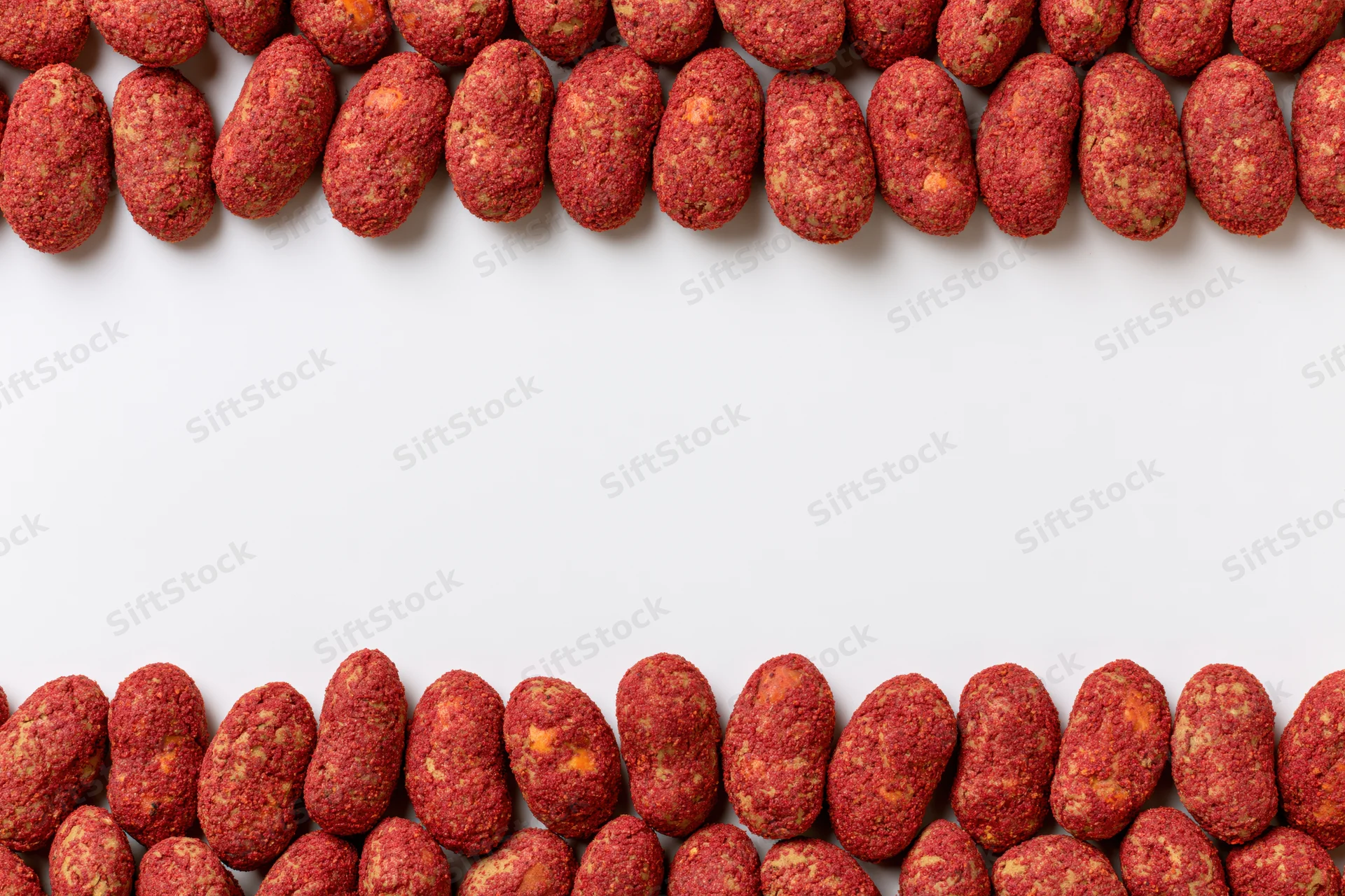 Red-coated peanuts with chili spice crust arranged in two rows at top and bottom of white surface