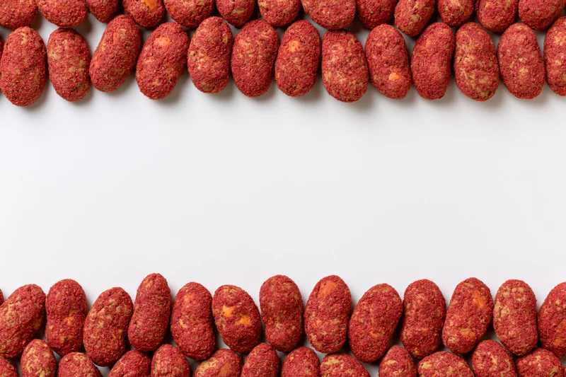 Red-coated peanuts with chili spice crust arranged in two rows at top and bottom of white surface