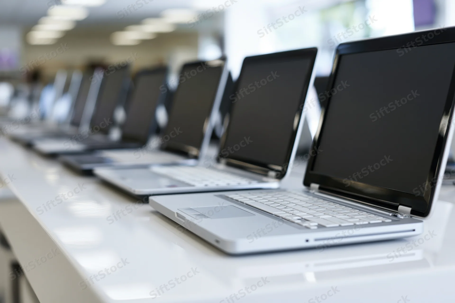 Row of open laptops with blank screens arranged on a white table in a retail showroom