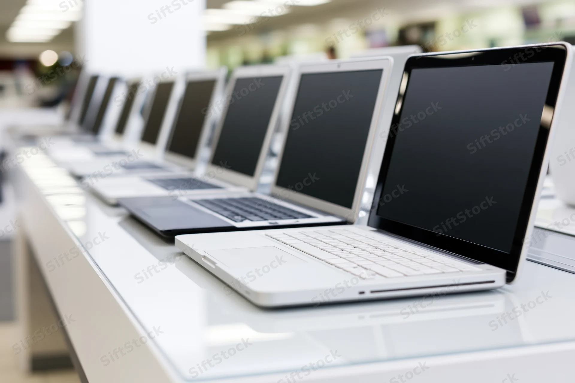 Row of open laptops with blank black screens displayed on a white counter in a retail store