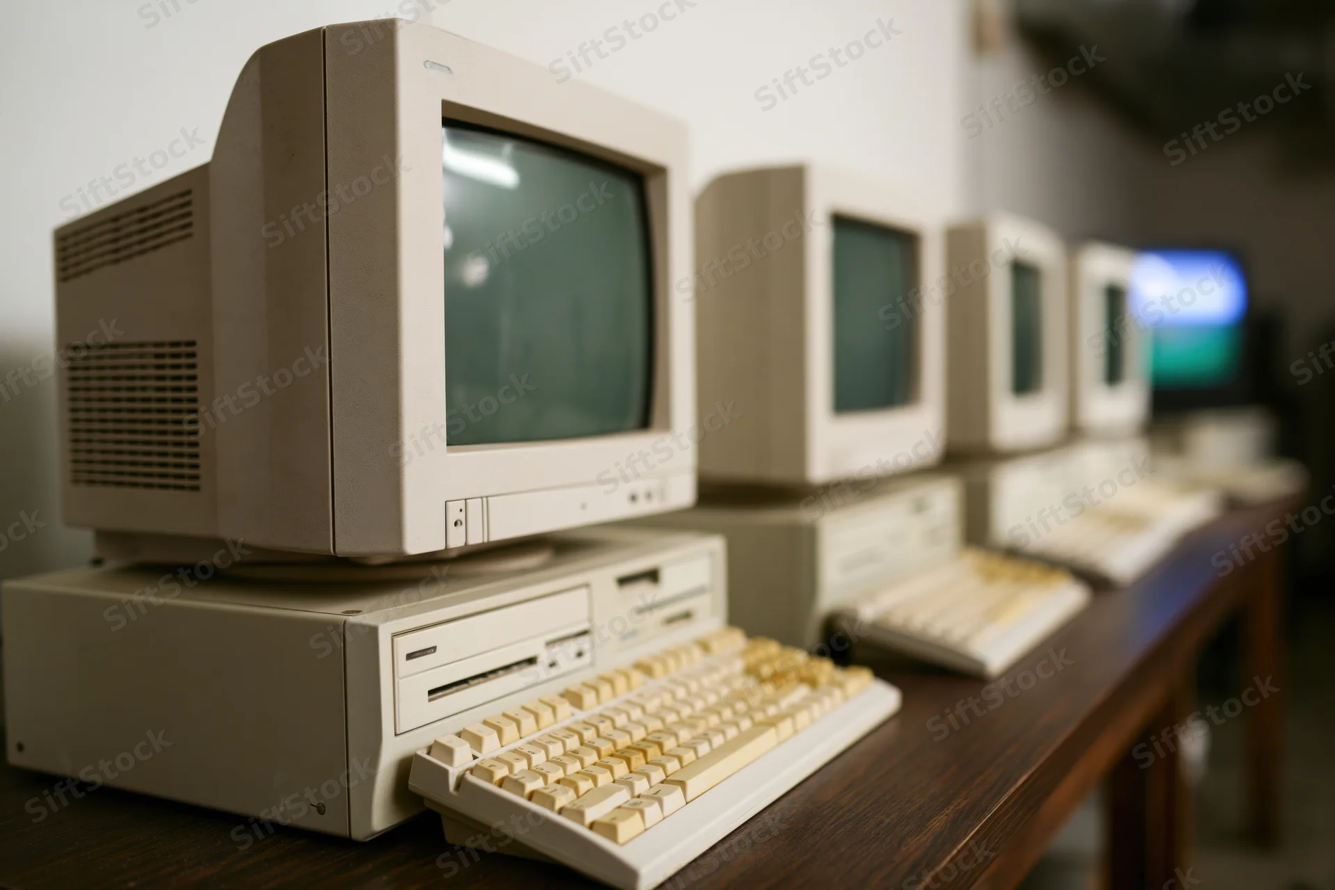 Row of vintage beige desktop computers with crt monitors and keyboards on wooden table