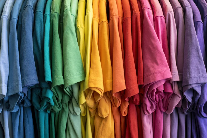 Rows of colorful cotton t-shirts hanging tightly packed on a rack in a retail display