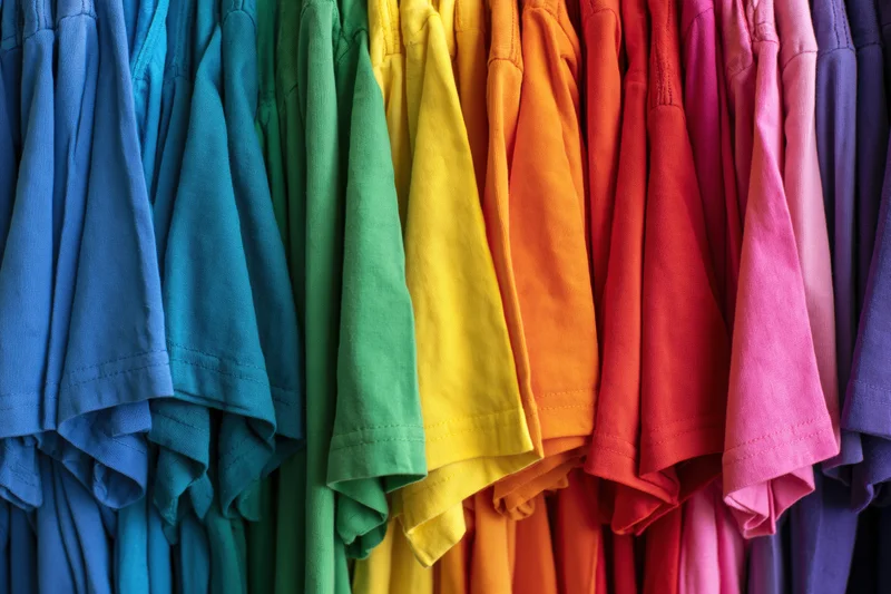 Rows of colorful cotton t-shirts hanging tightly packed on a rack in a retail store display