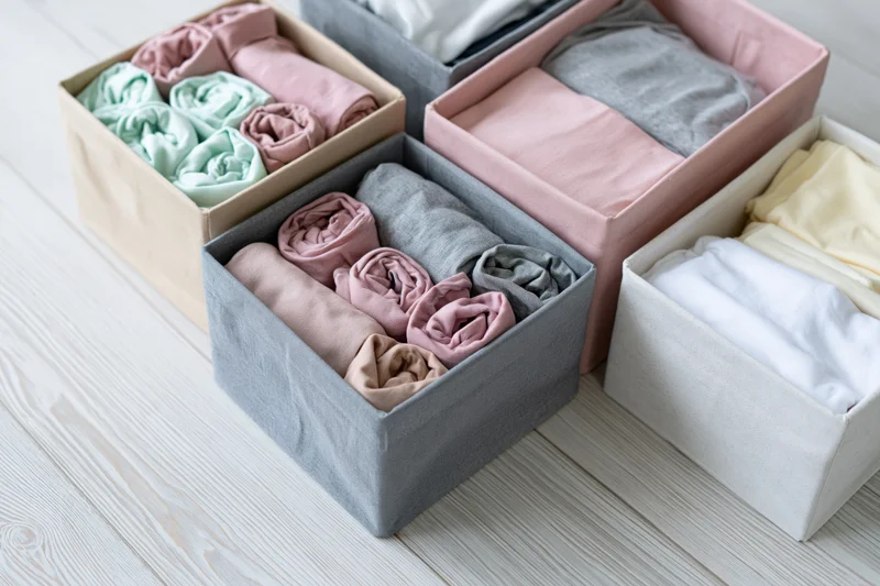 Fabric storage boxes filled with rolled and folded clothing arranged on a wooden floor