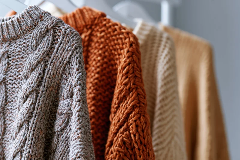 Several knit sweaters hanging on a clothing rack in a closet