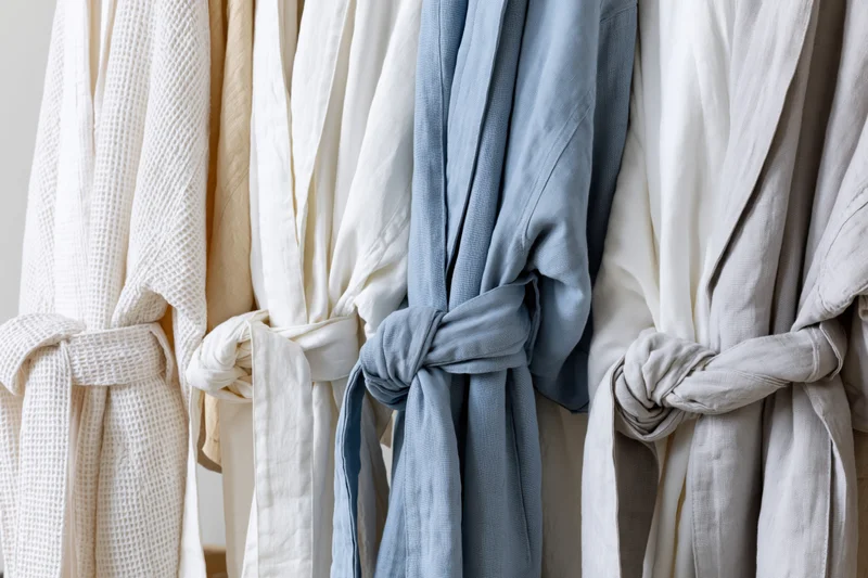 Several bathrobes in neutral tones hanging on a rack in a home setting