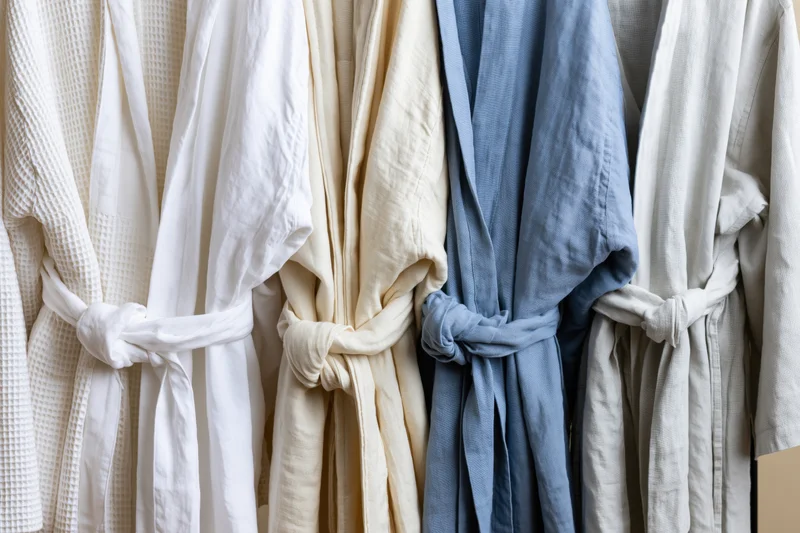 Several linen and cotton bathrobes hanging on a rack in neutral tones