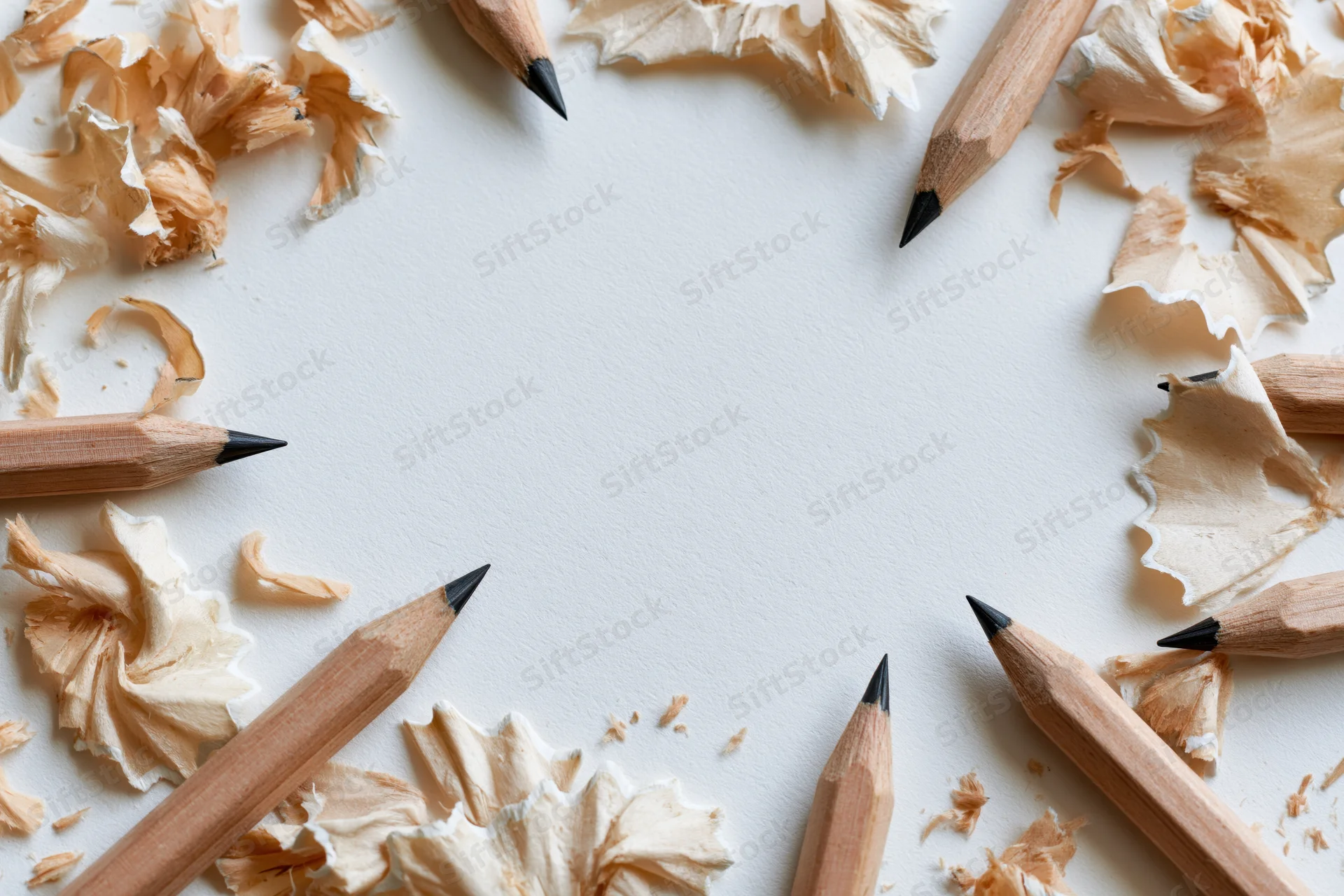 Sharpened graphite pencils and curled wood shavings arranged in a circle on a white surface with central copyspace