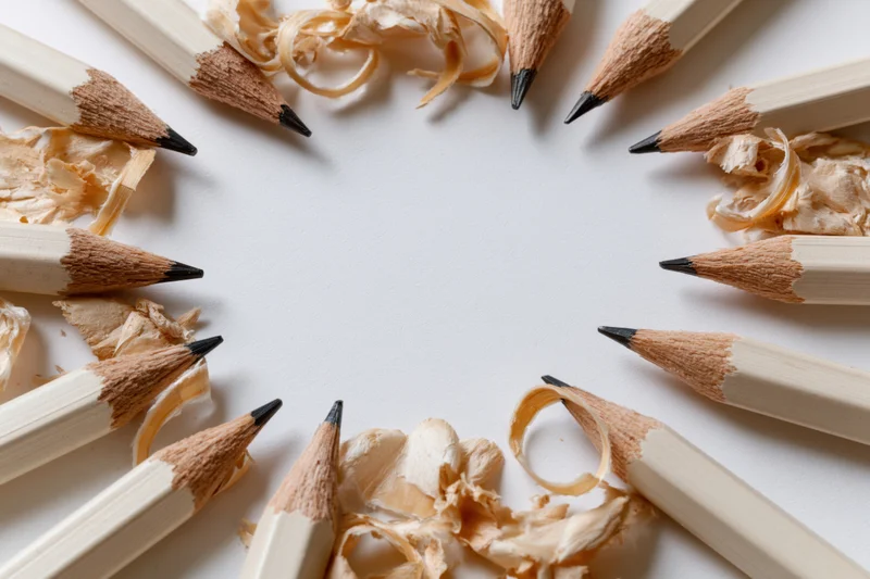 Sharpened graphite pencils arranged in a circle with wood shavings on white surface