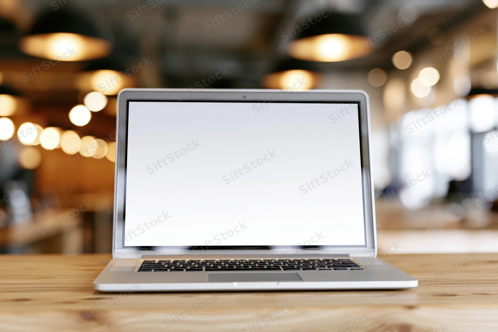 Silver laptop with blank white screen open on wooden desk in cafe interior