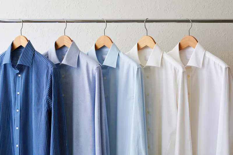 Six men's dress shirts in blue and white hanging on wooden hangers on a metal rack