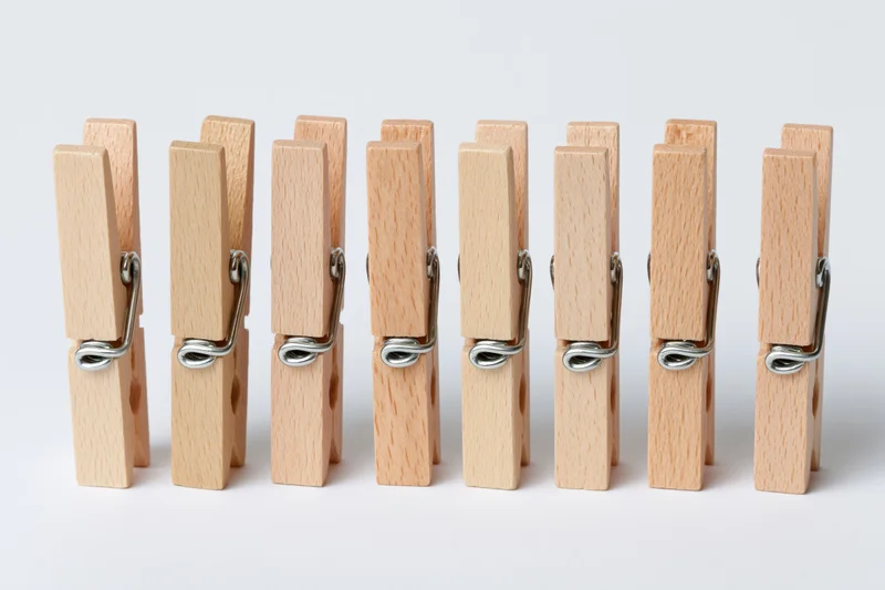 Six wooden clothespins standing upright in a row on a white background