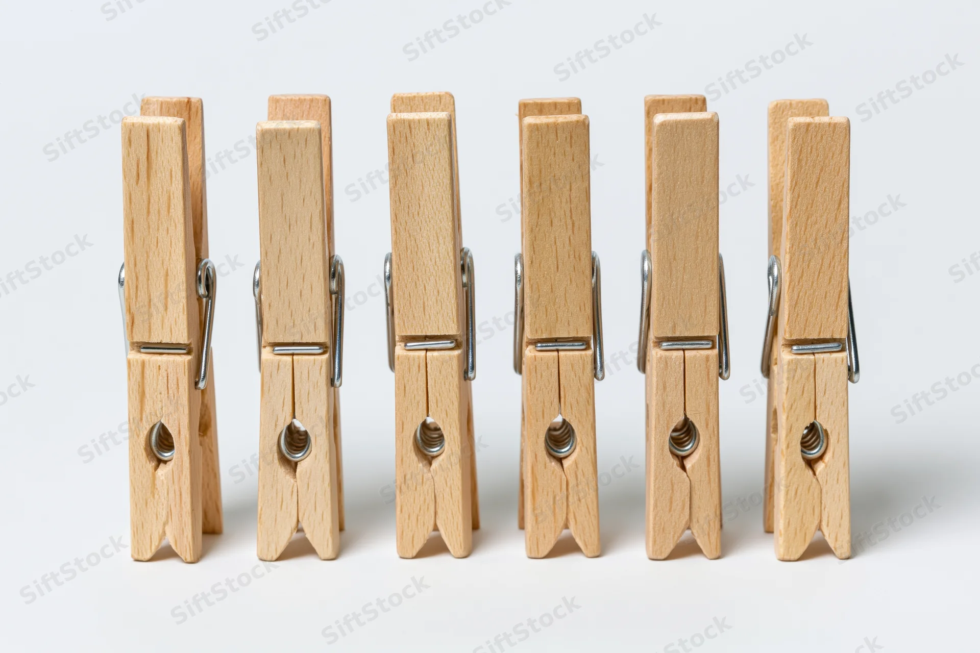 Six wooden clothespins standing upright in a row on a white surface