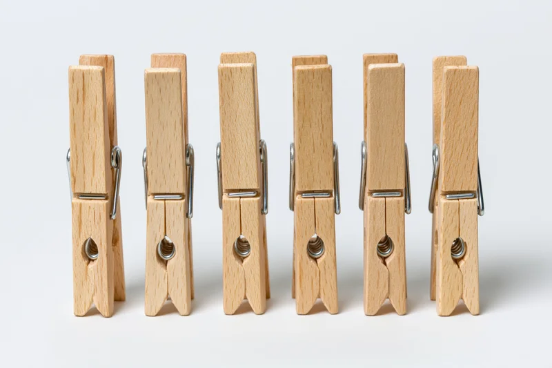 Six wooden clothespins standing upright in a row on a white surface