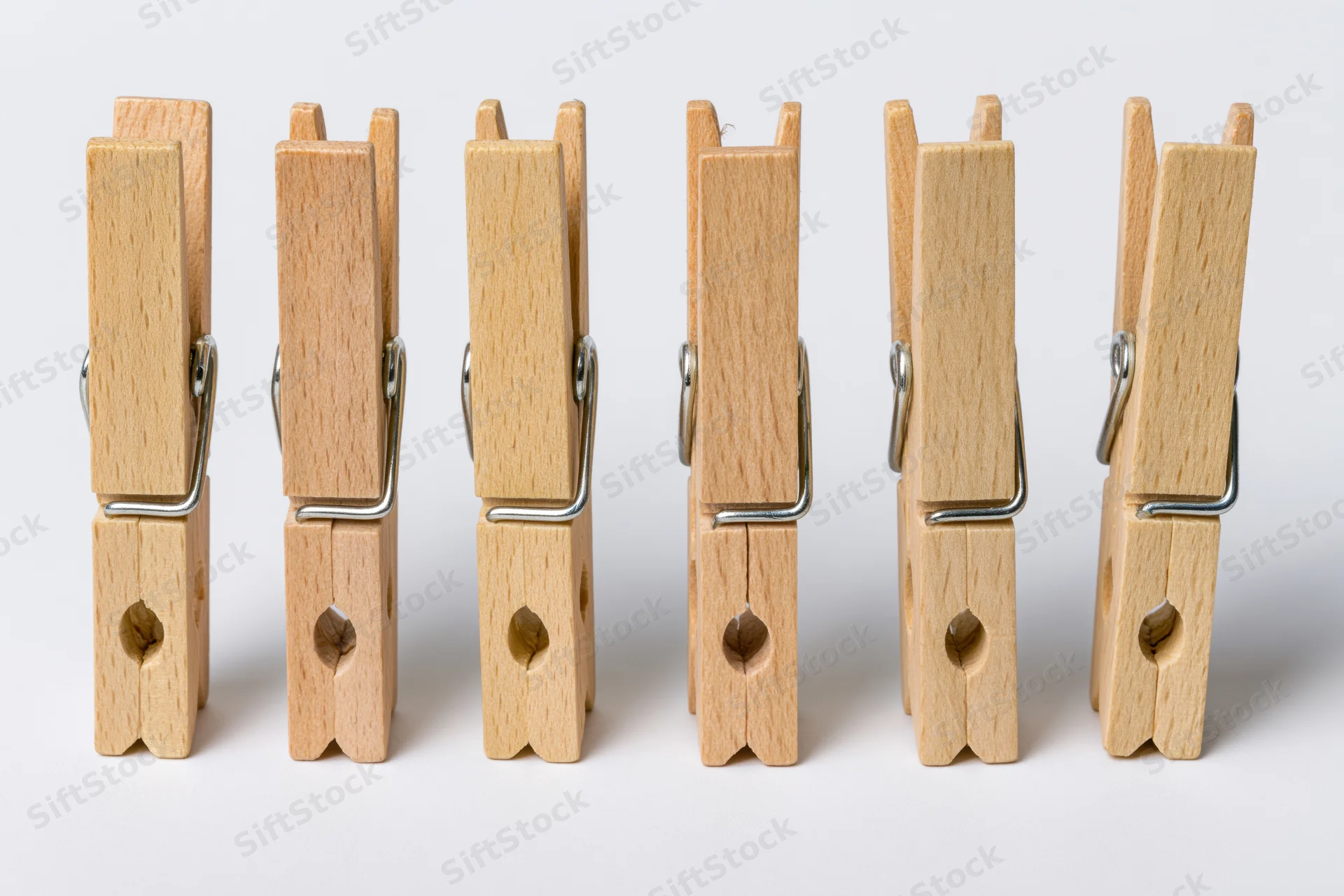 Six wooden clothespins standing upright in a row on a white surface