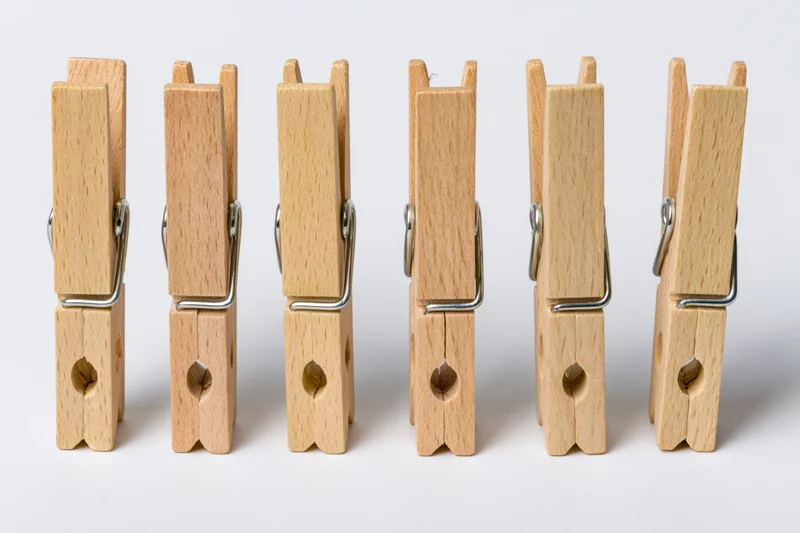 Six wooden clothespins standing upright in a row on a white surface