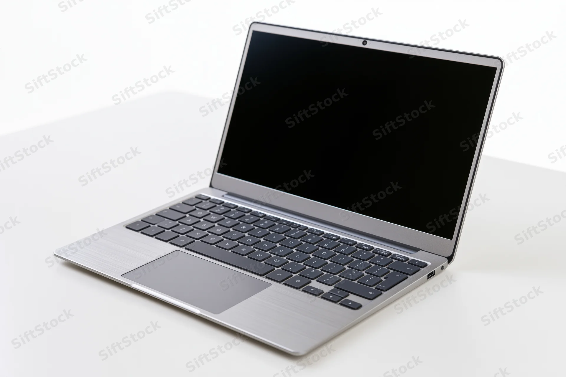 Open silver aluminum laptop with blank black screen on white surface
