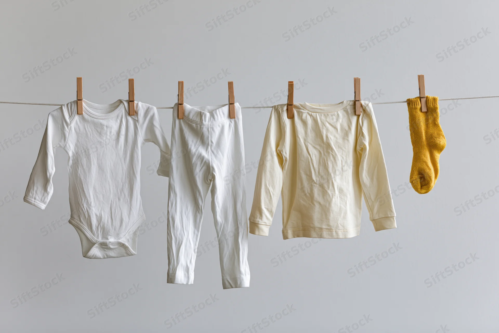 Baby clothes hanging on a clothesline with wooden pegs against a plain background