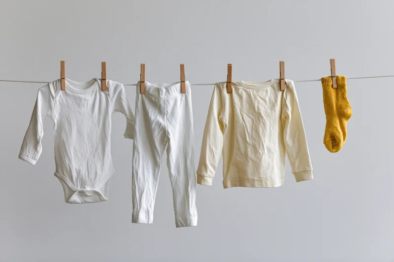 Baby clothes hanging on a clothesline with wooden pegs against a plain background