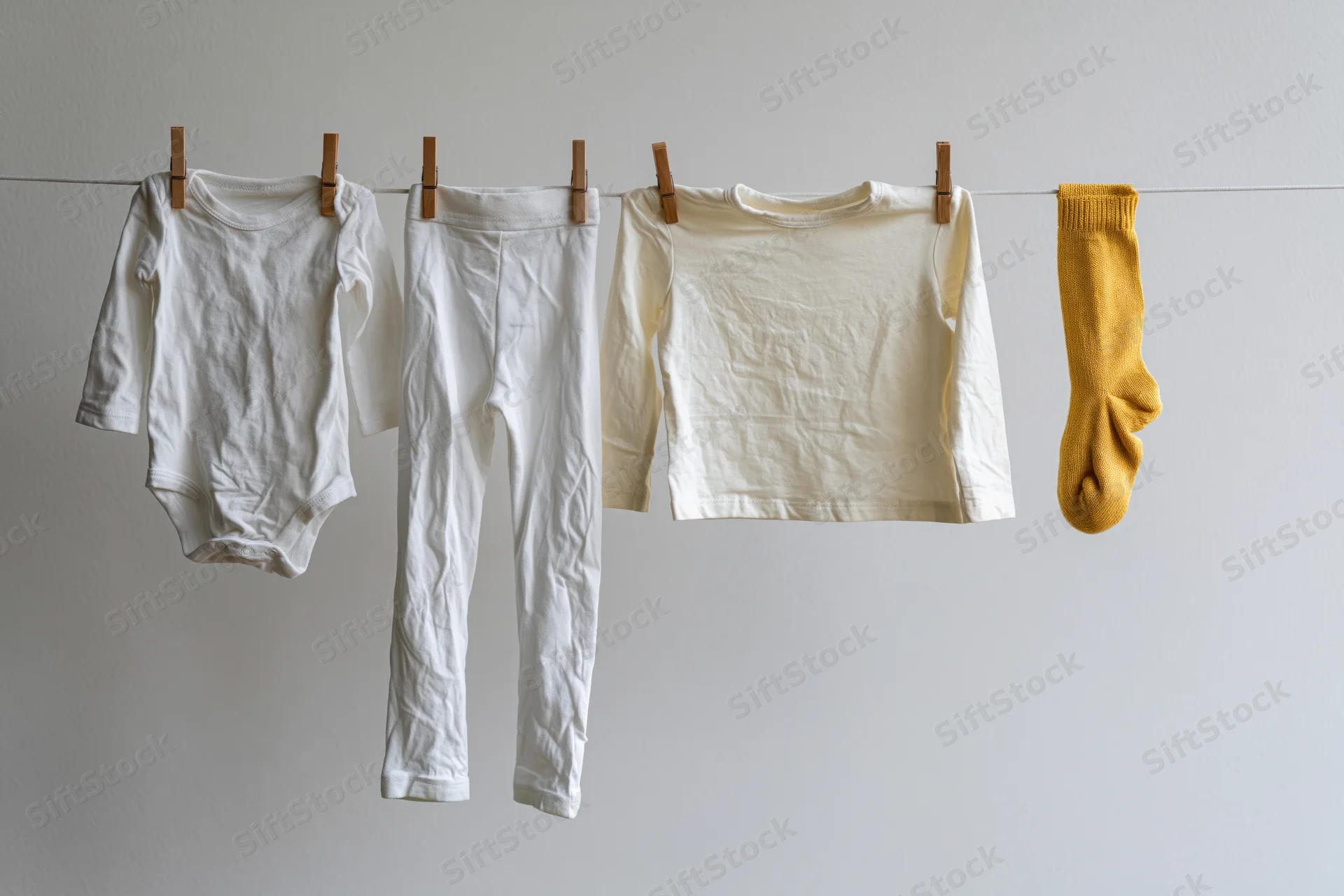 Baby clothes hanging on a clothesline against a white wall