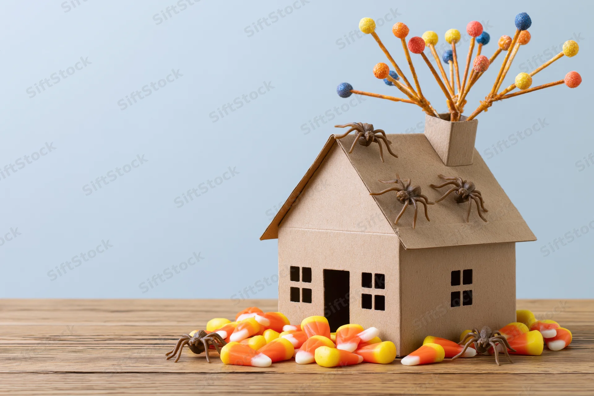 Cardboard miniature house decorated with spiders and candy corn on wooden surface for halloween