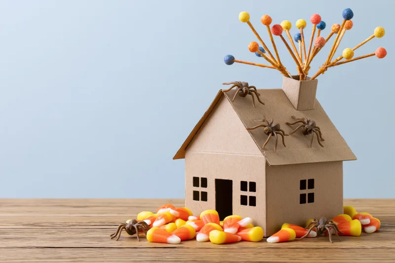 Cardboard miniature house decorated with spiders and candy corn on wooden surface for halloween